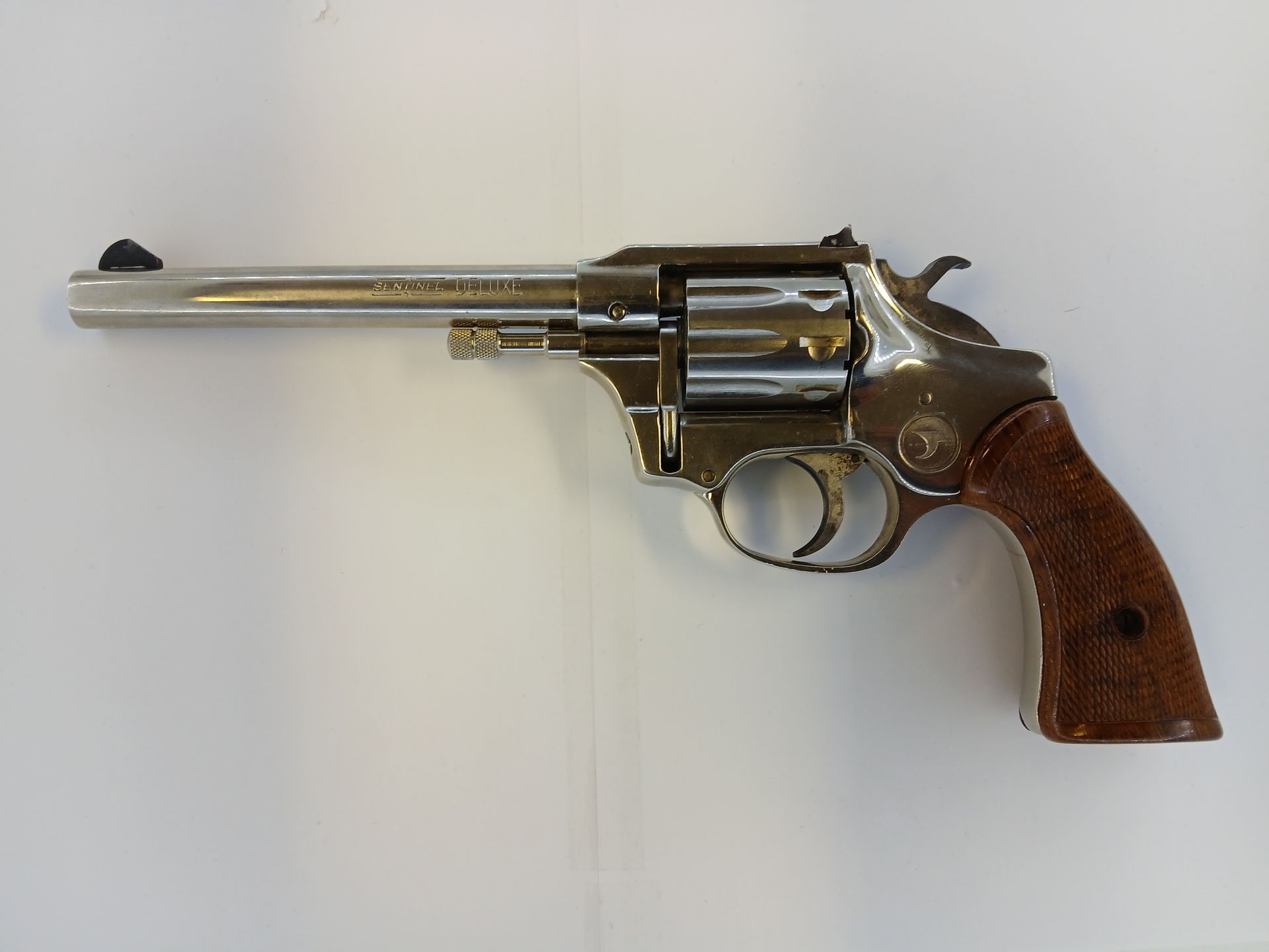 Revolver argenté brillant avec poignée marron sur une surface blanche.