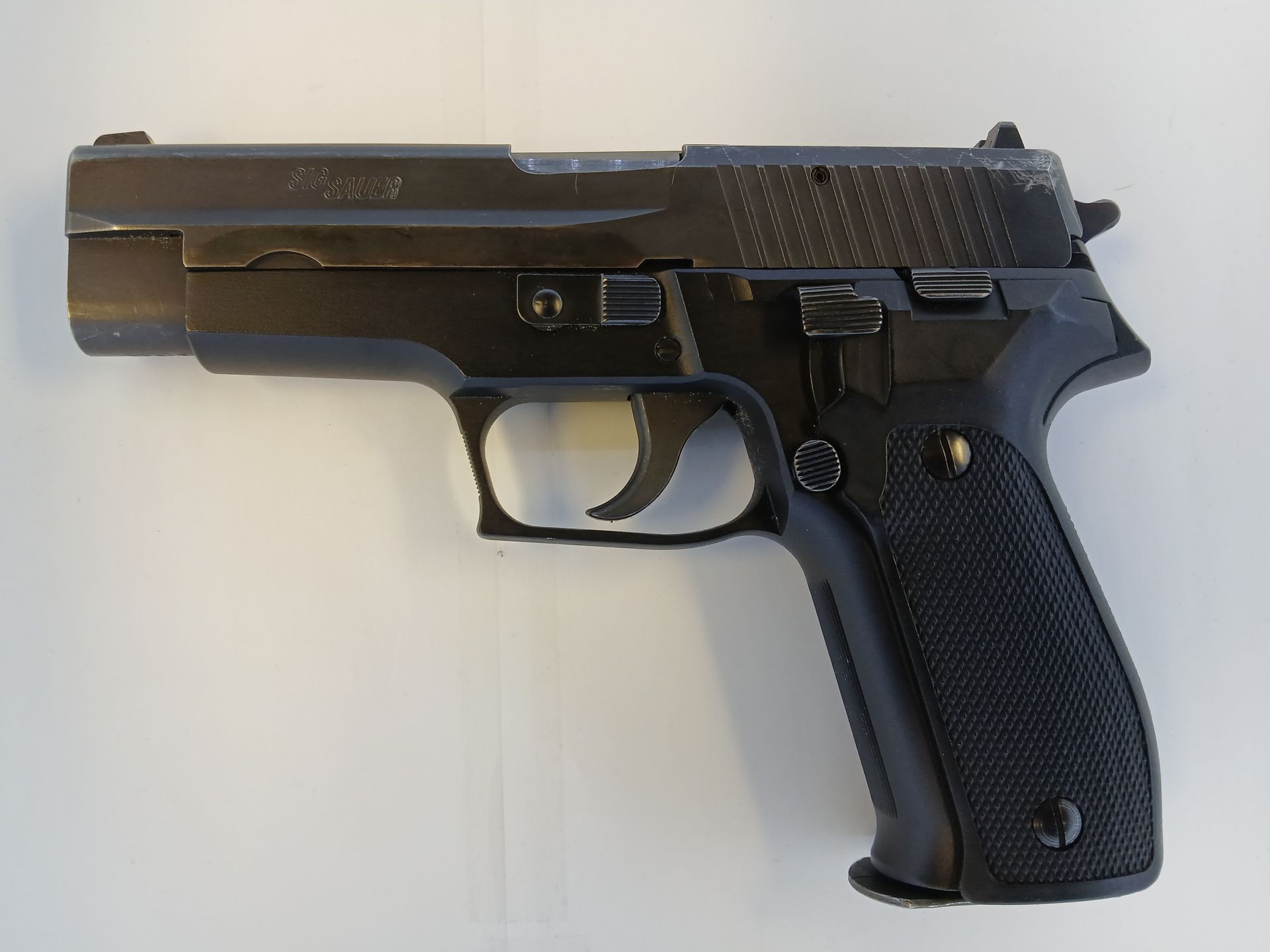 Pistolet noir avec poignée texturée, posé sur une surface blanche.