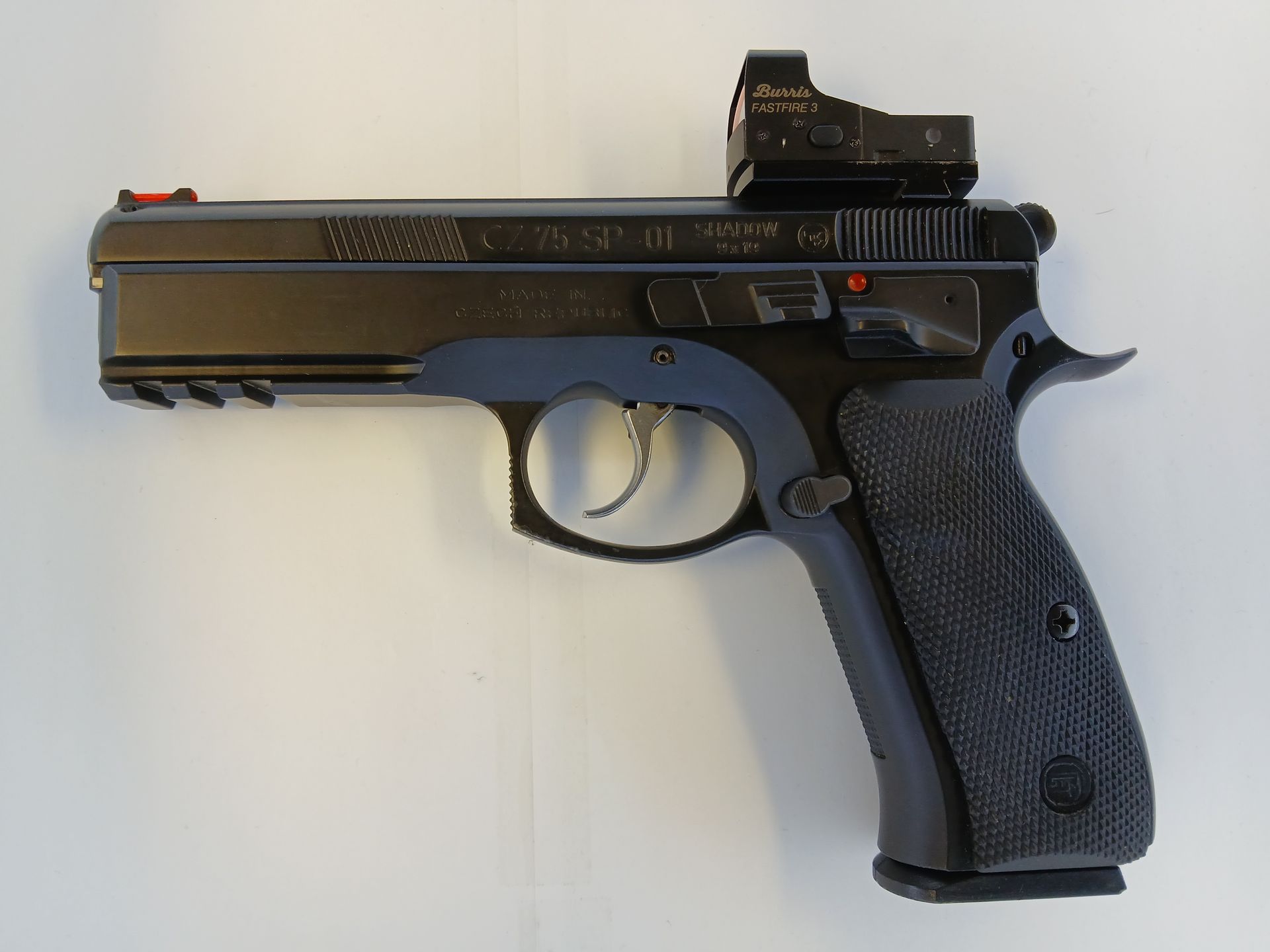 Pistolet noir et bleu avec viseur point rouge ; monté sur une surface blanche.