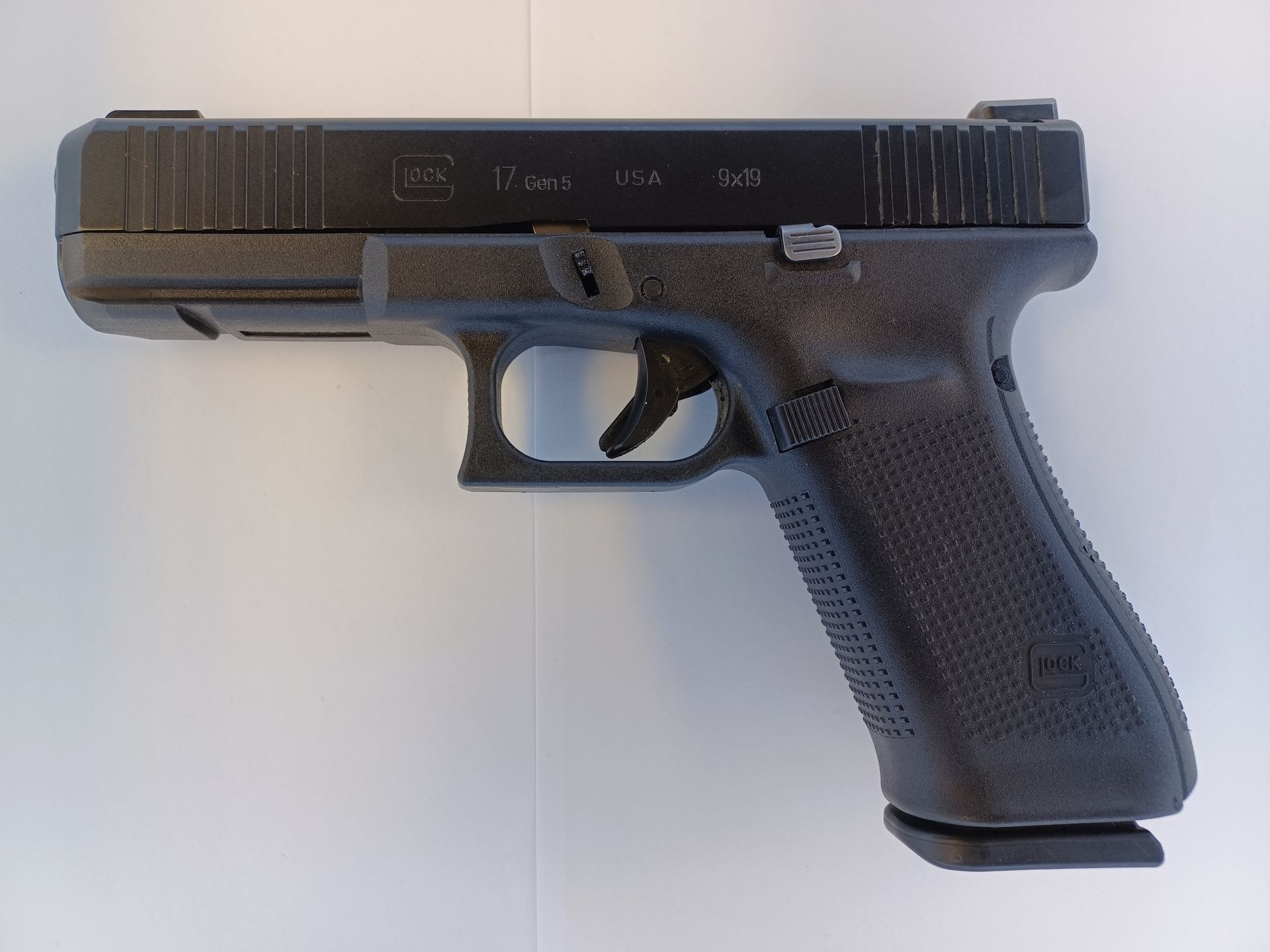 Pistolet Glock noir sur une surface blanche, incliné vers la droite.