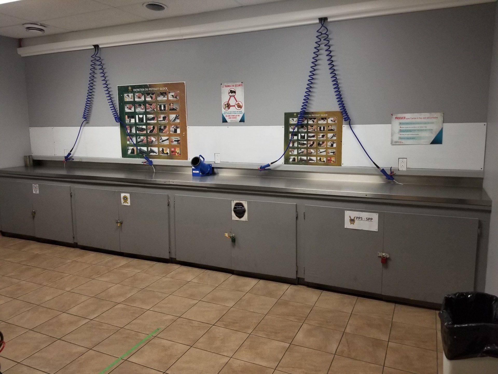 Une station de lavage avec des armoires grises, un comptoir en acier inoxydable et des tuyaux enroulés bleus.