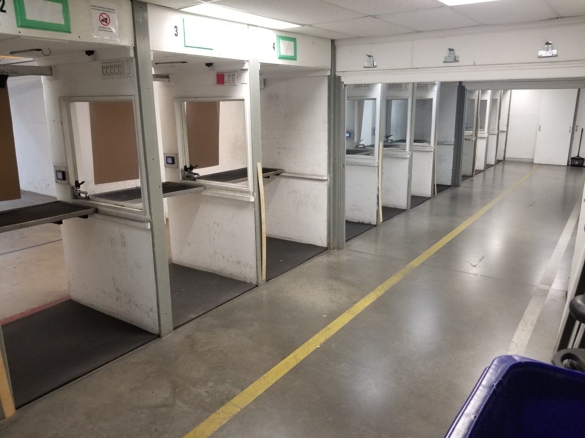 Stand de tir avec couloirs de tir individuels. Sol en béton, murs blancs et ligne jaune.