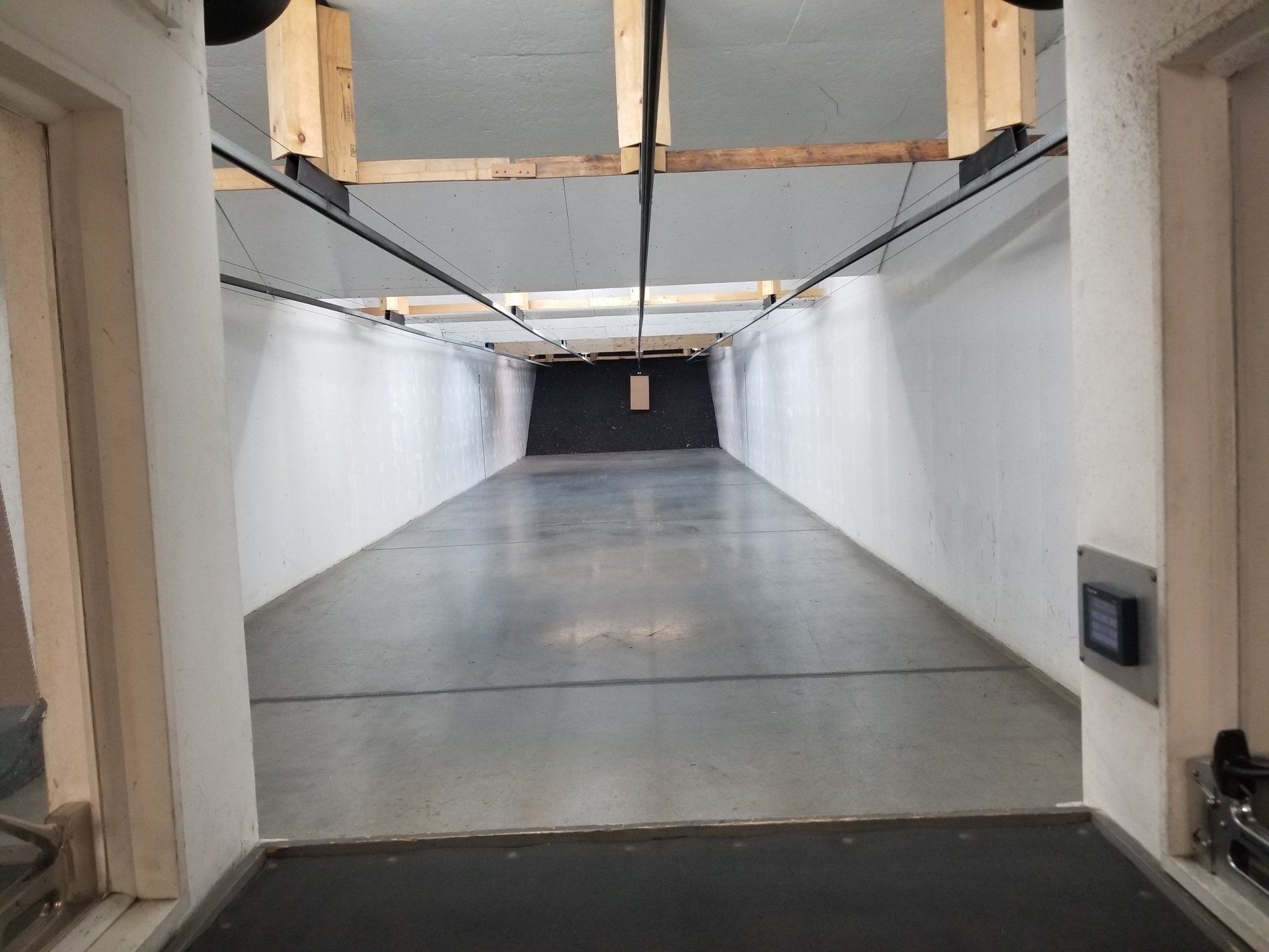Stand de tir intérieur vide avec des murs blancs, un sol noir et une cible au bout.