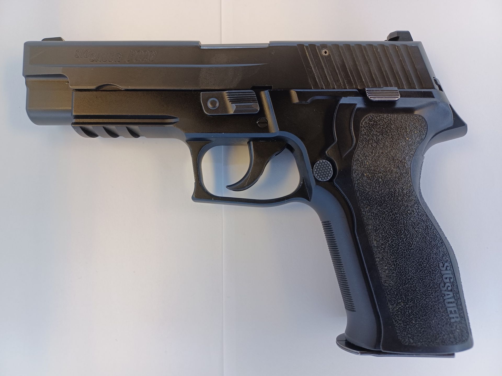 Pistolet Sig Sauer P226 noir sur une surface blanche, montrant le côté avec la poignée et la gâchette.