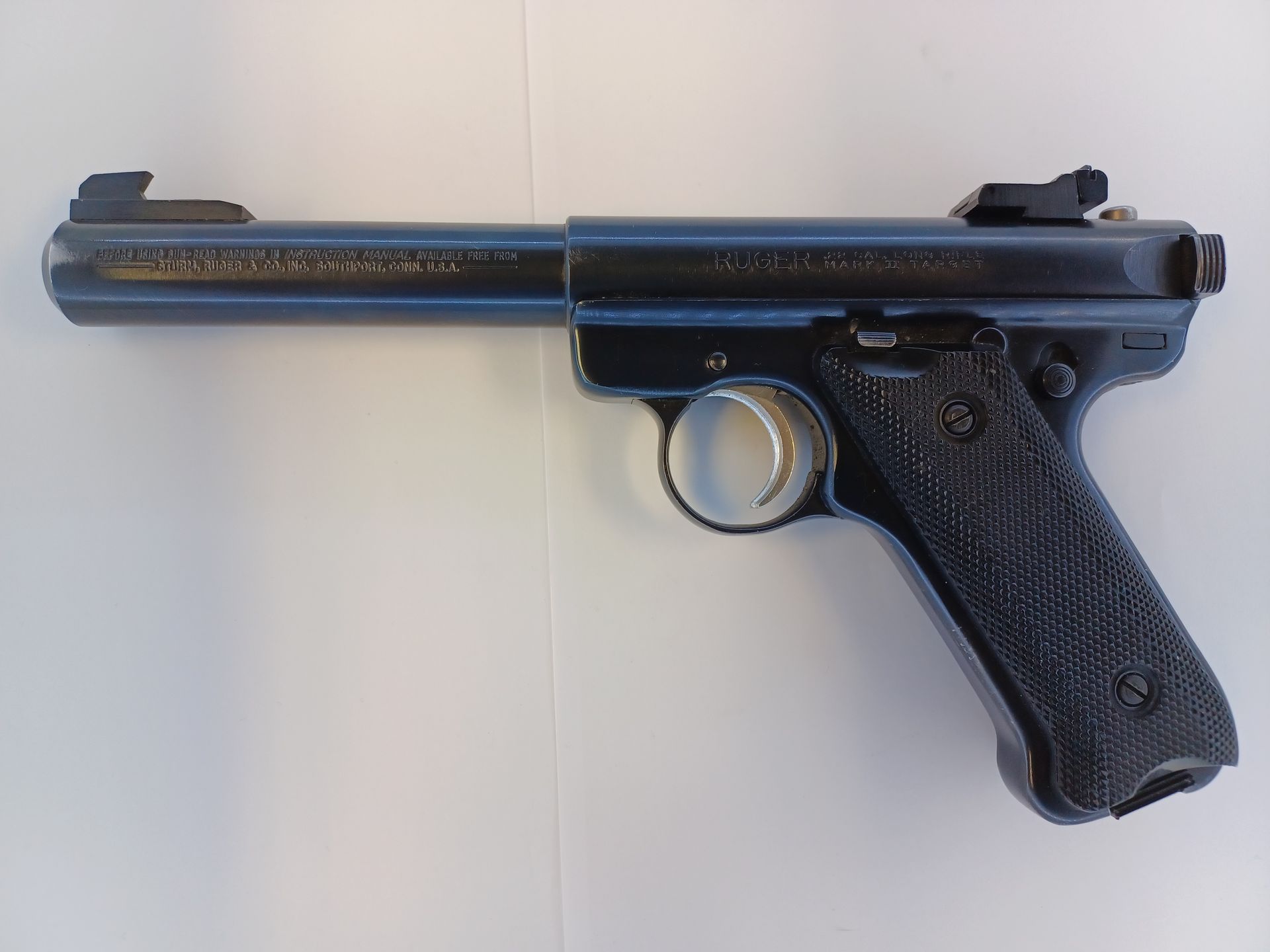 Un pistolet Ruger Mark IV noir sur une surface blanche, vu de côté.