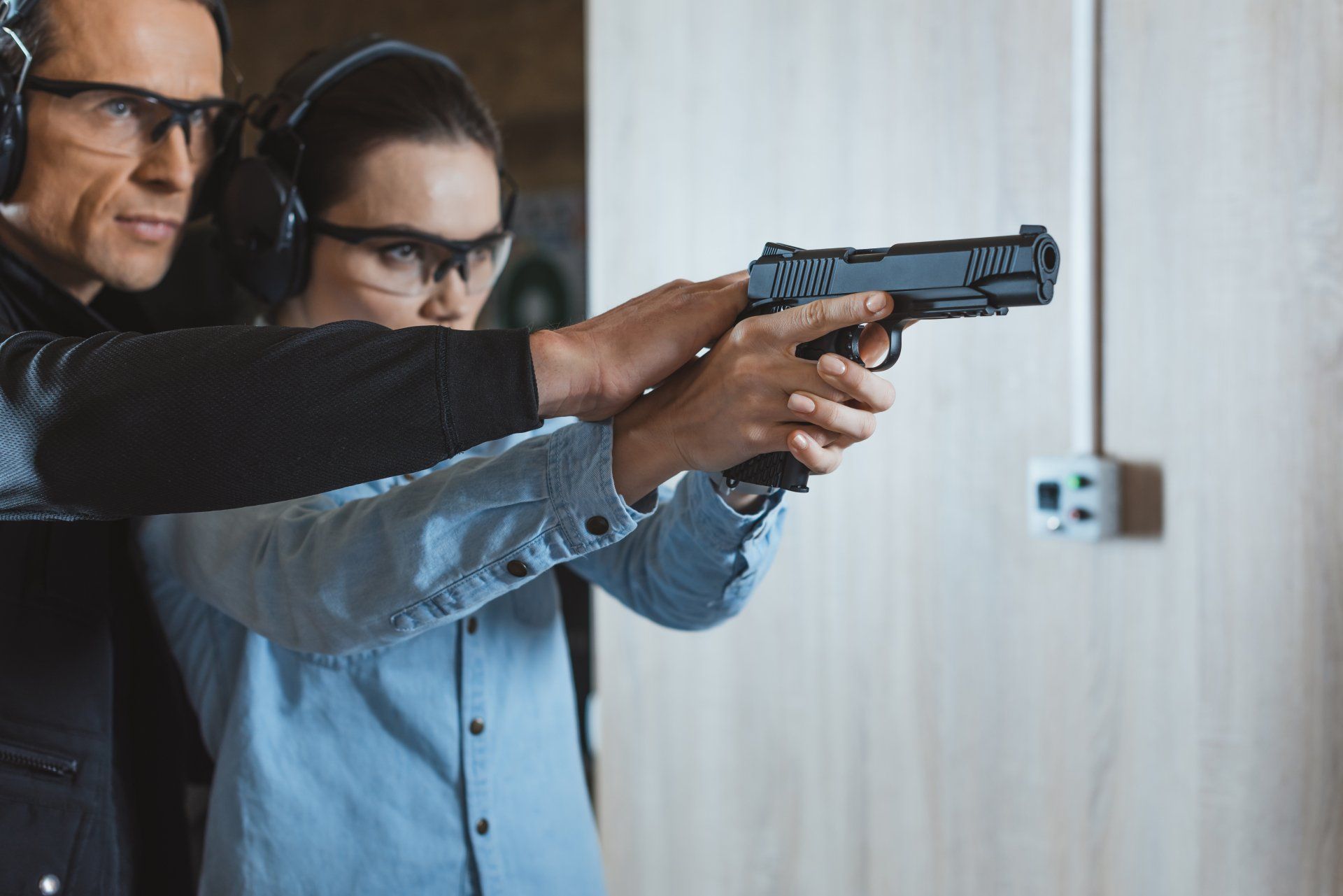 Un homme aide une femme à tirer avec une arme de poing dans un champ de tir ; tous deux portent des protections pour les yeux et les oreilles.
