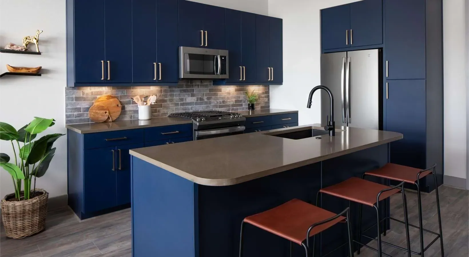 Modern kitchen with dark blue cabinets, stainless steel appliances, and a large island with bar stools at Bellrock Sawyer Yards offers apartments in Houston, TX.