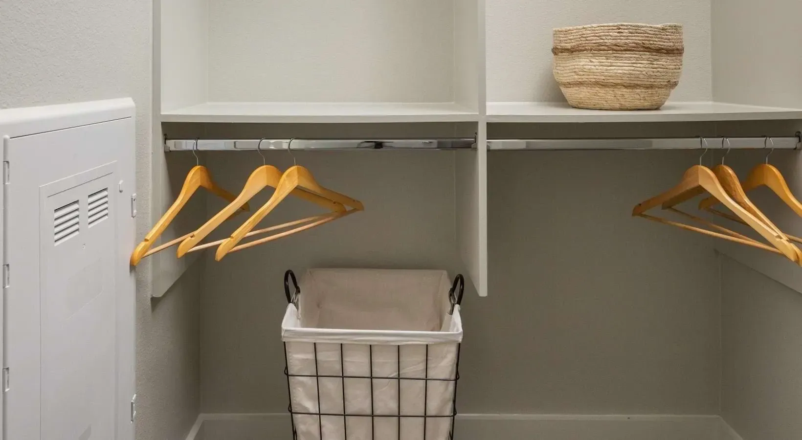 Spacious closet with built-in shelves, hanging rods, wooden hangers, and a laundry basket.