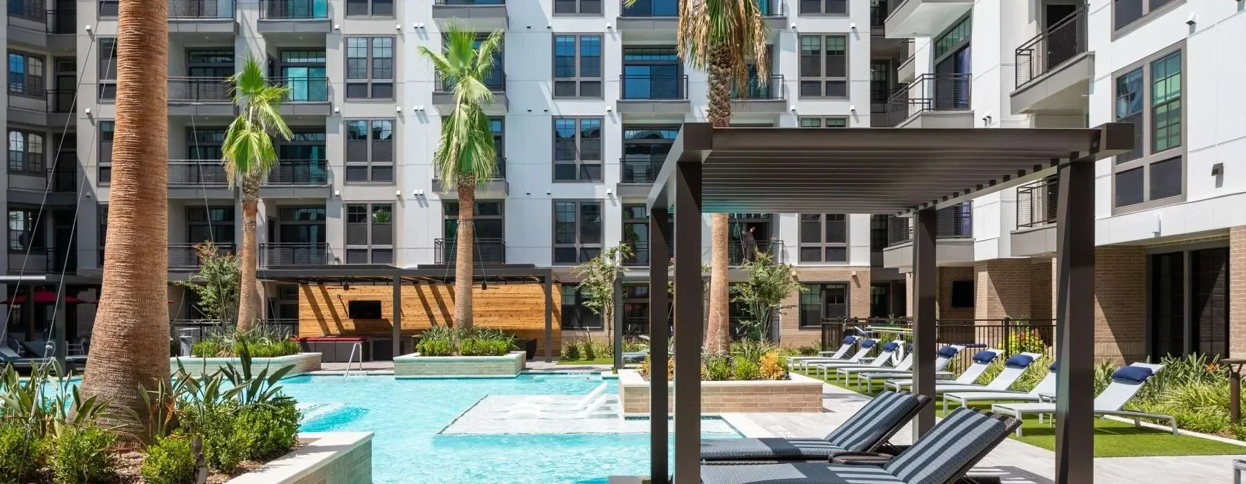 Luxury apartment complex pool area with lounge chairs and palm trees.