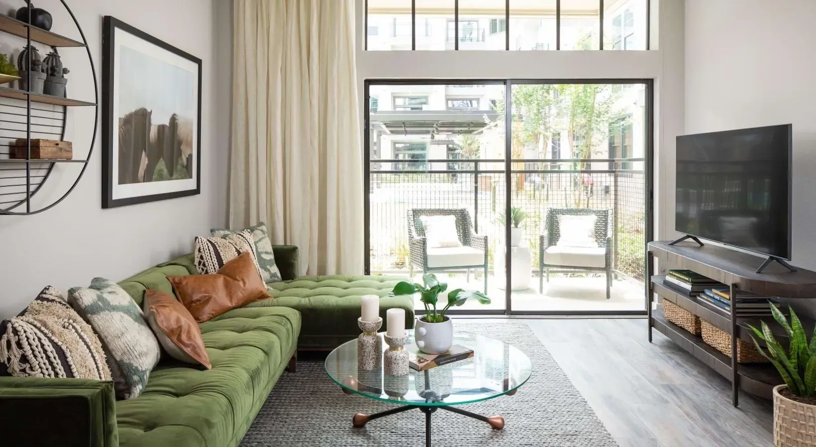 Stylish living room with a large green sectional sofa, glass coffee table, and TV.