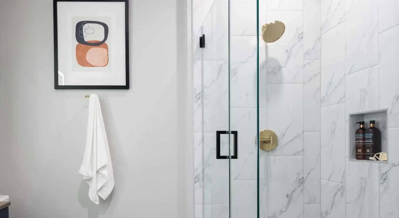 Modern bathroom with marble tile shower, gold fixtures, and abstract art.