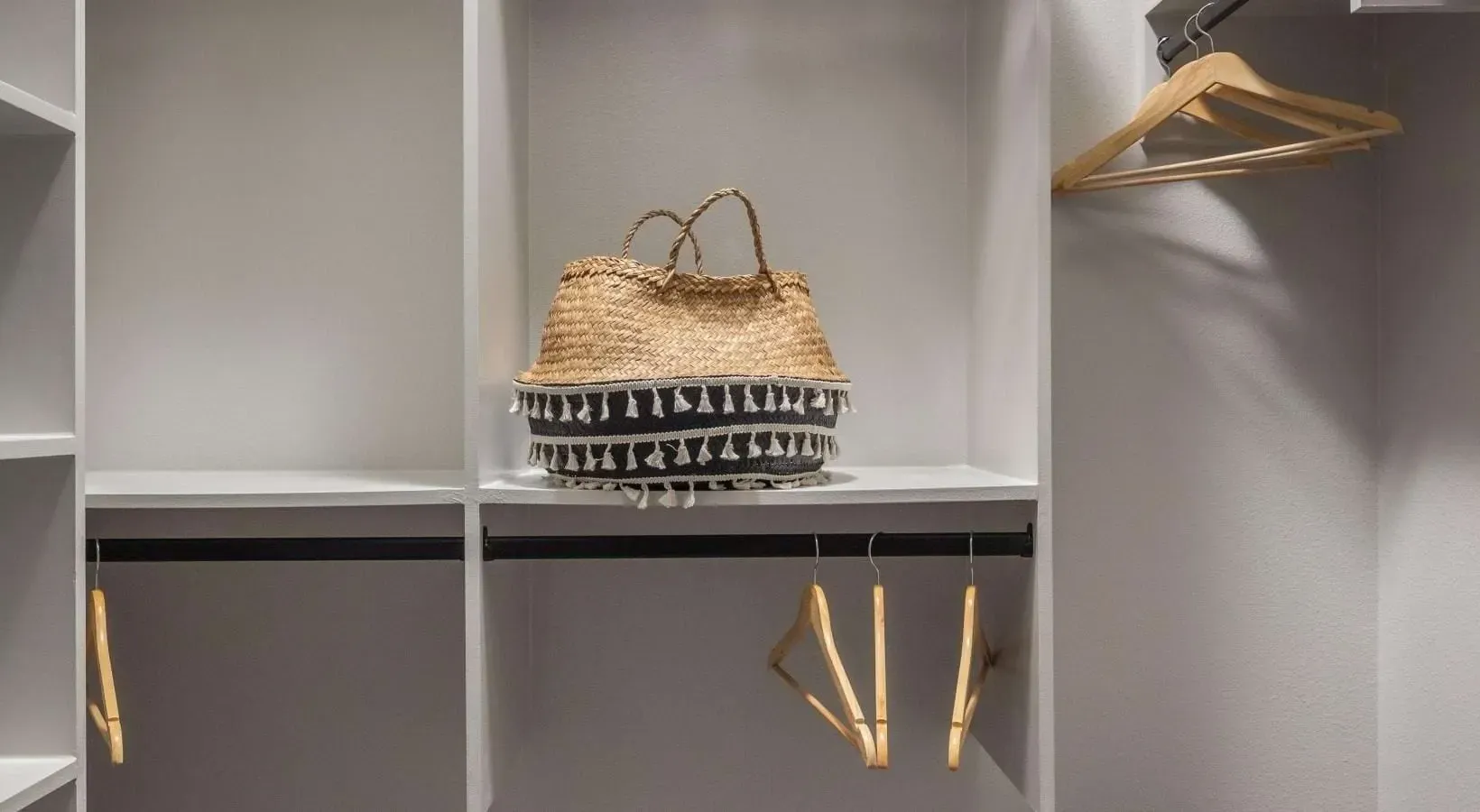 Closet interior with shelving and hanging rods, featuring a decorative straw basket.