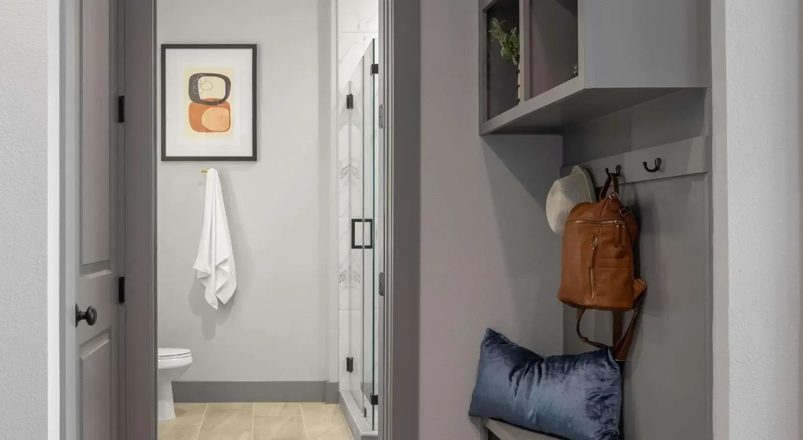 Modern bathroom with a walk-in shower and a toilet, next to a mudroom area with a backpack and hat.