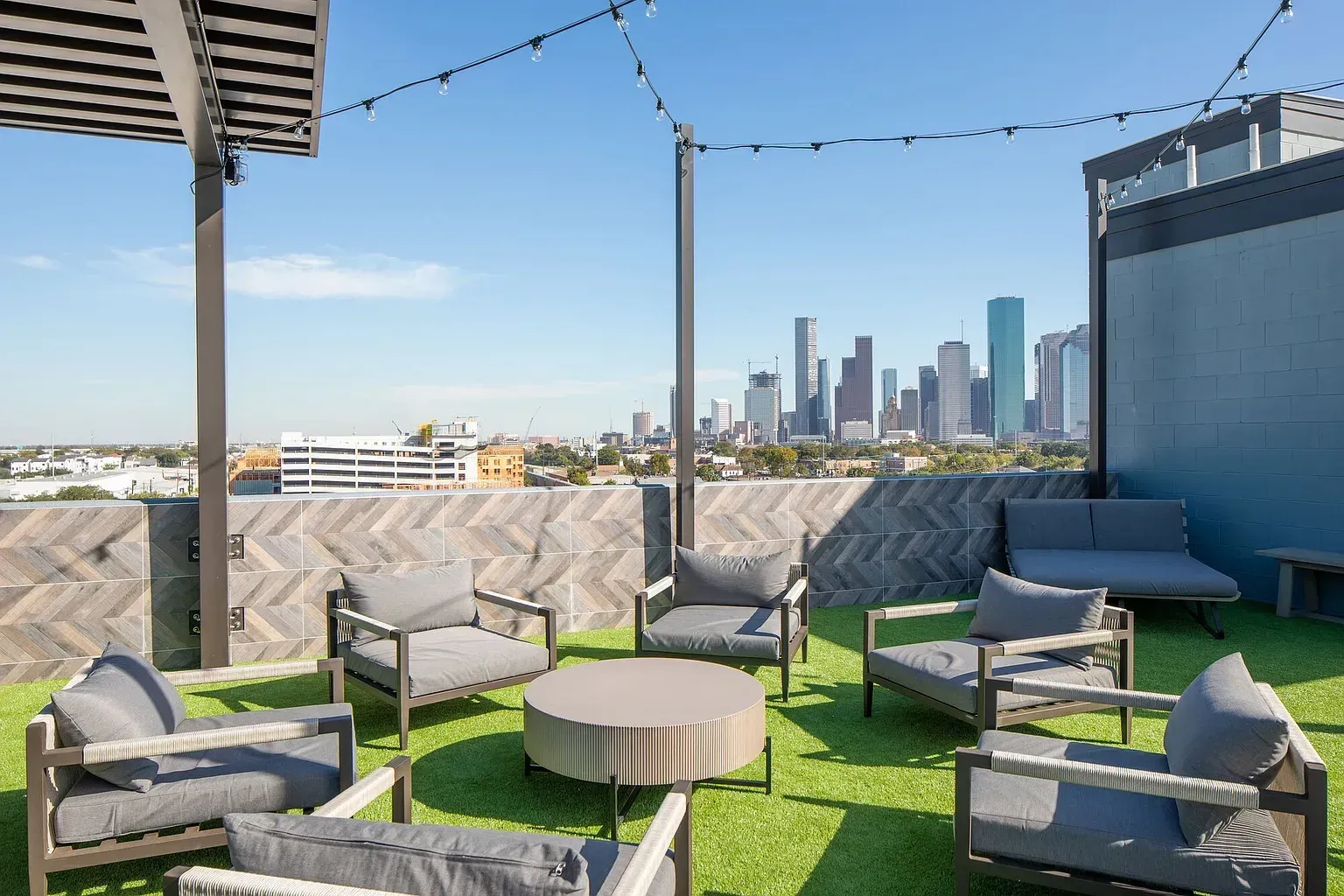 Rooftop patio with gray seating, round table, green turf, and city skyline in the background