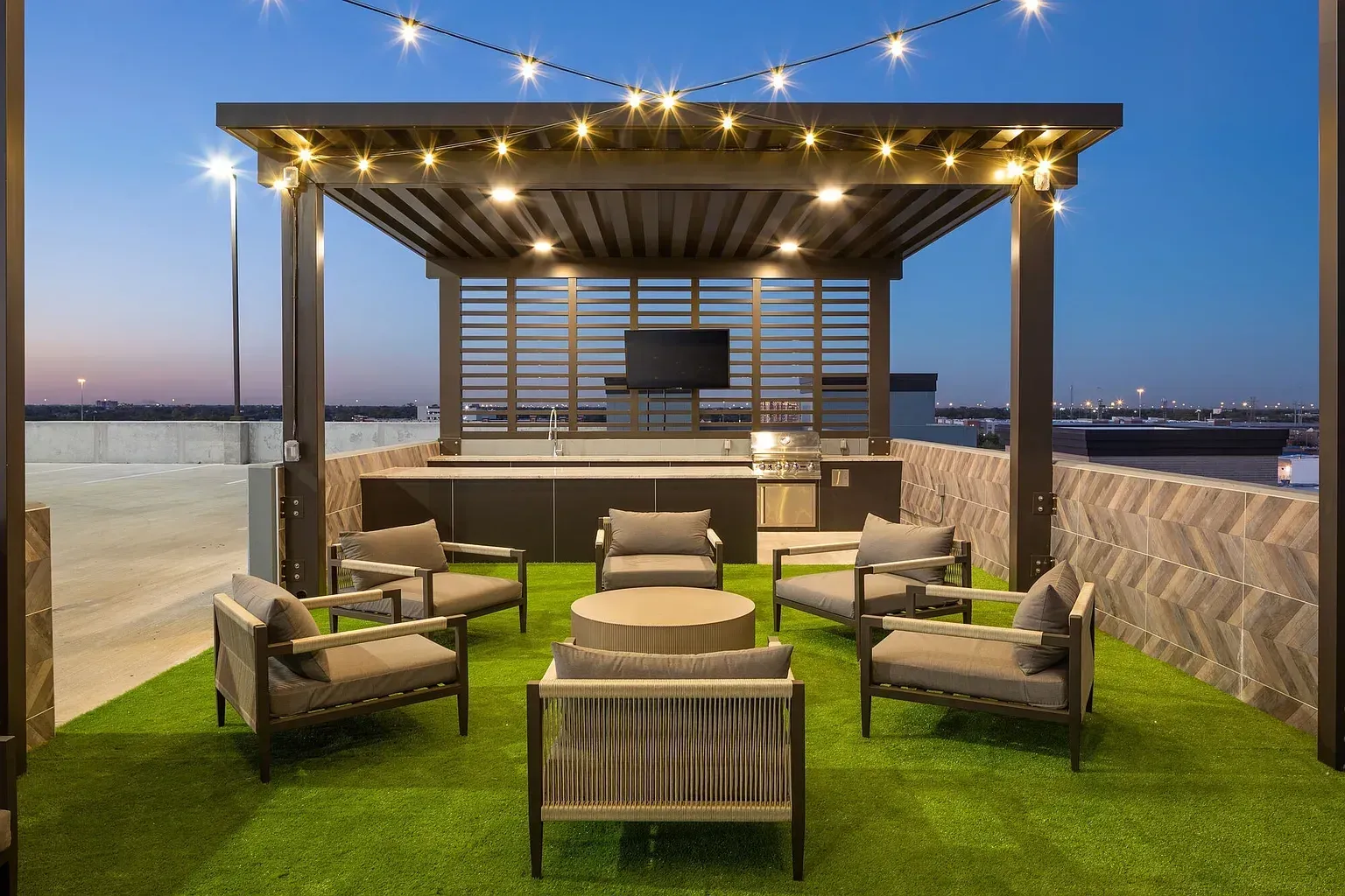 Rooftop lounge with wicker chairs, green turf, and string lights at sunset