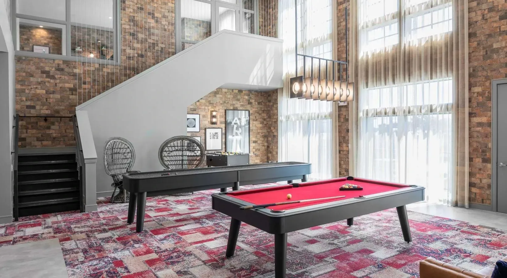 Billiard table and shuffleboard in a common area with a staircase and brick wall.