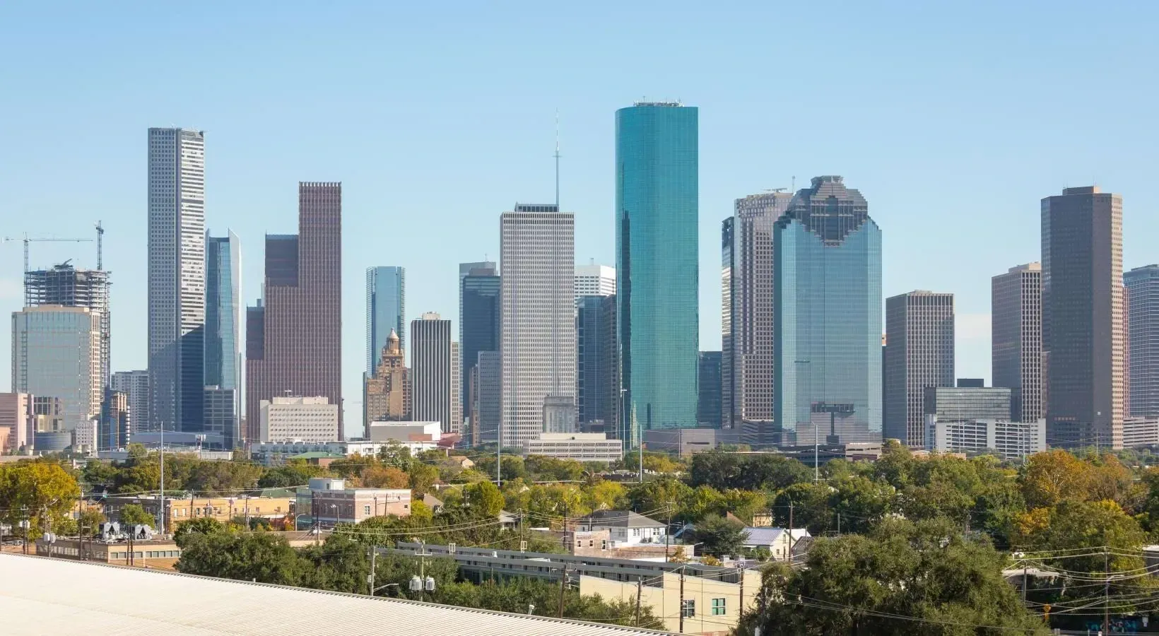 Skyline of downtown Houston with skyscrapers and trees in the foreground.