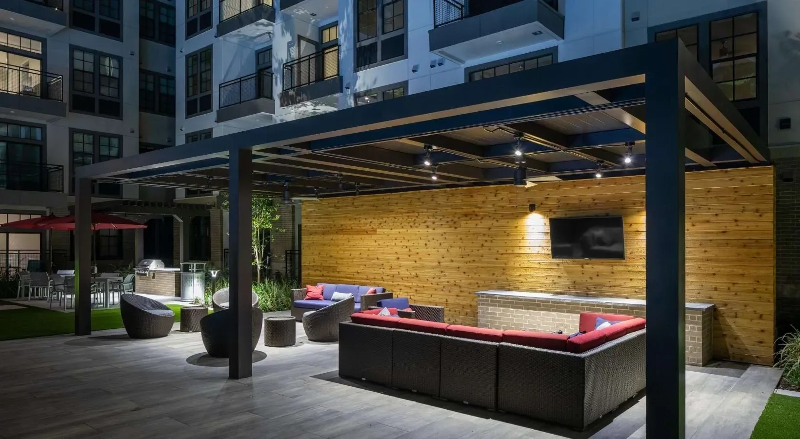 Outdoor patio lounge area with couches, chairs, a TV, and grilling station.