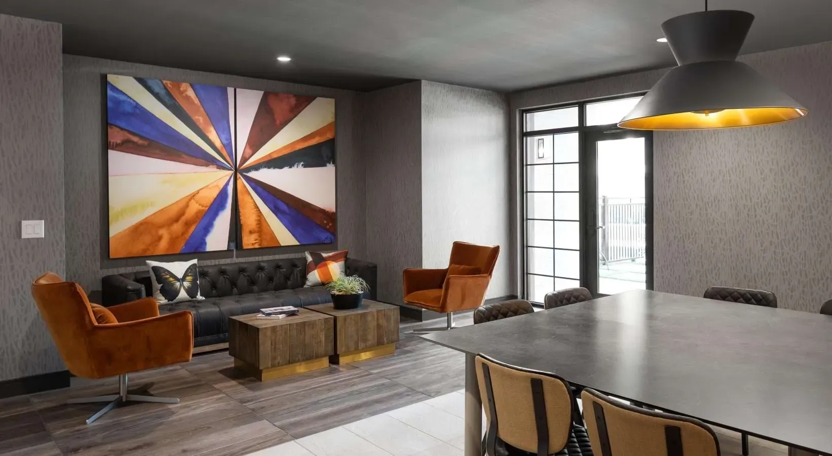 Modern lounge area with tufted sofa, orange accent chairs, and a large abstract painting.