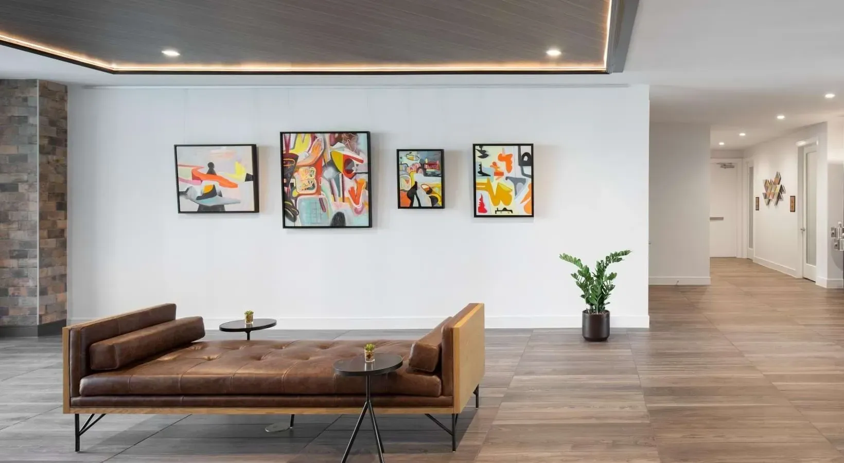 Modern lobby with a brown leather chaise lounge, abstract art, and a plant in a stylish common area.