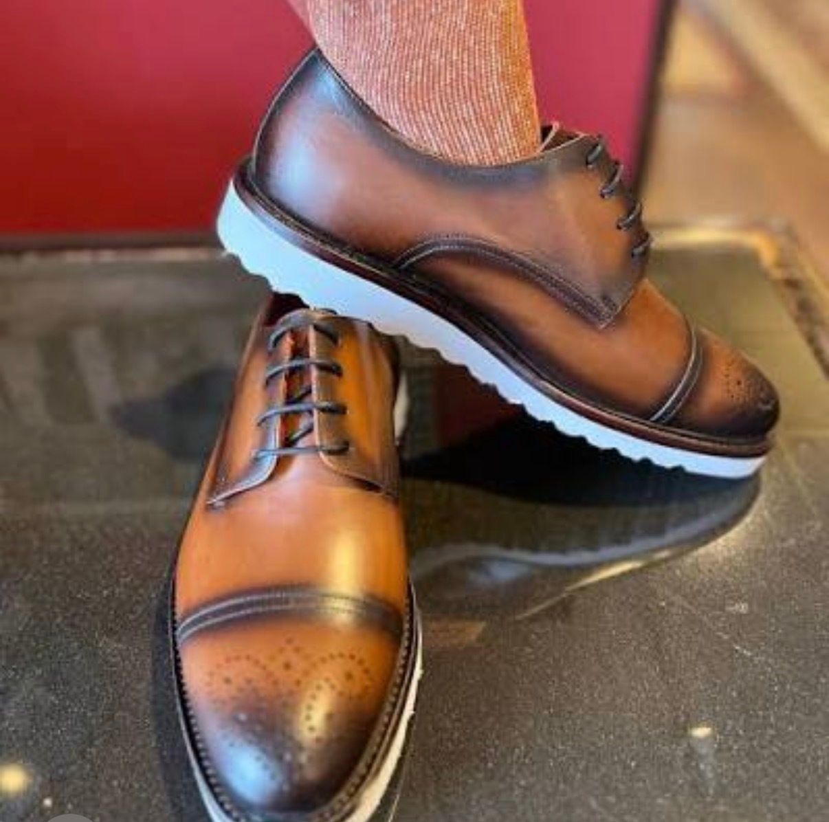 Two-tone brown leather dress shoes with black toe caps, one crossed over the other.