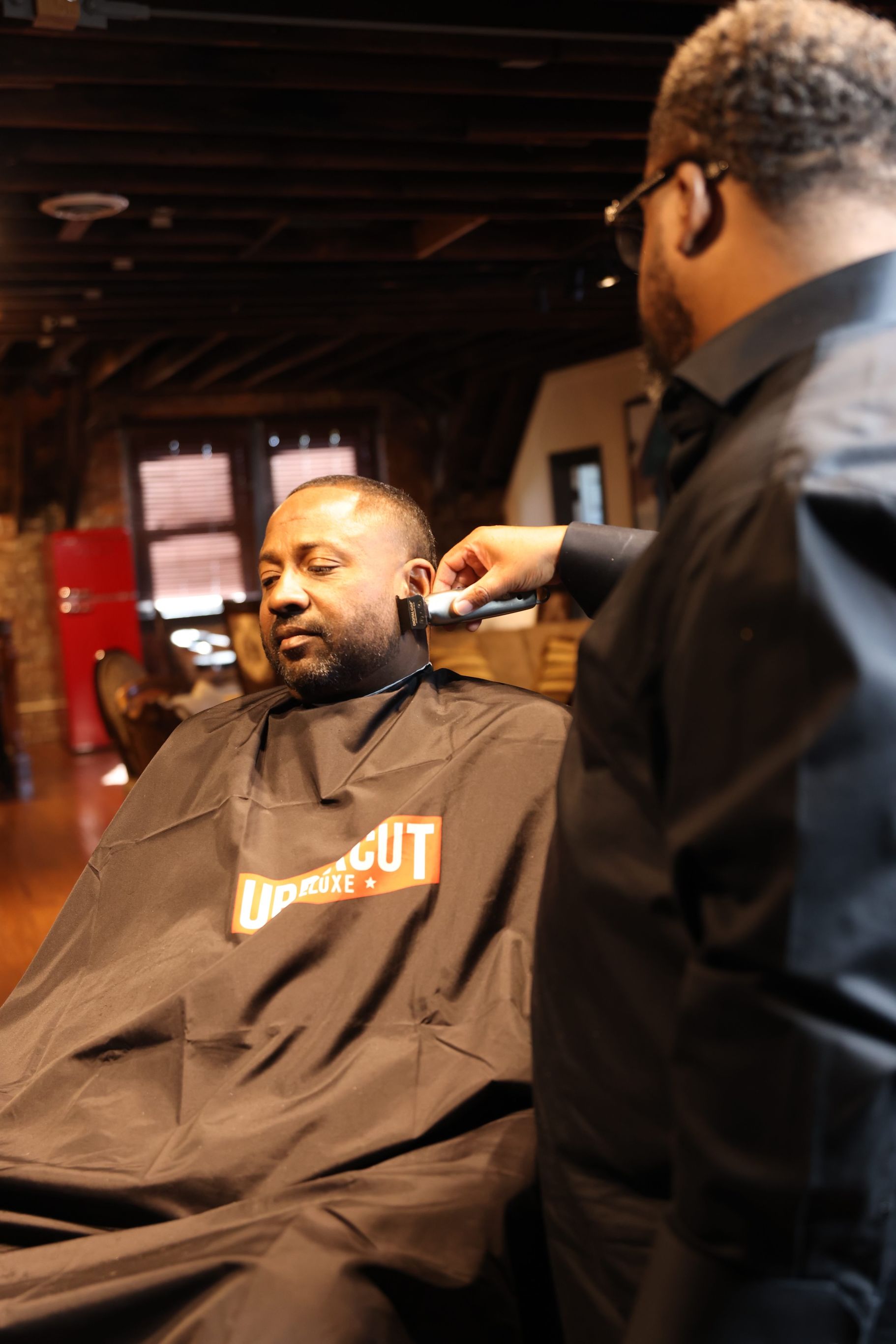 Barber trims a seated client’s hair in a dim barbershop.