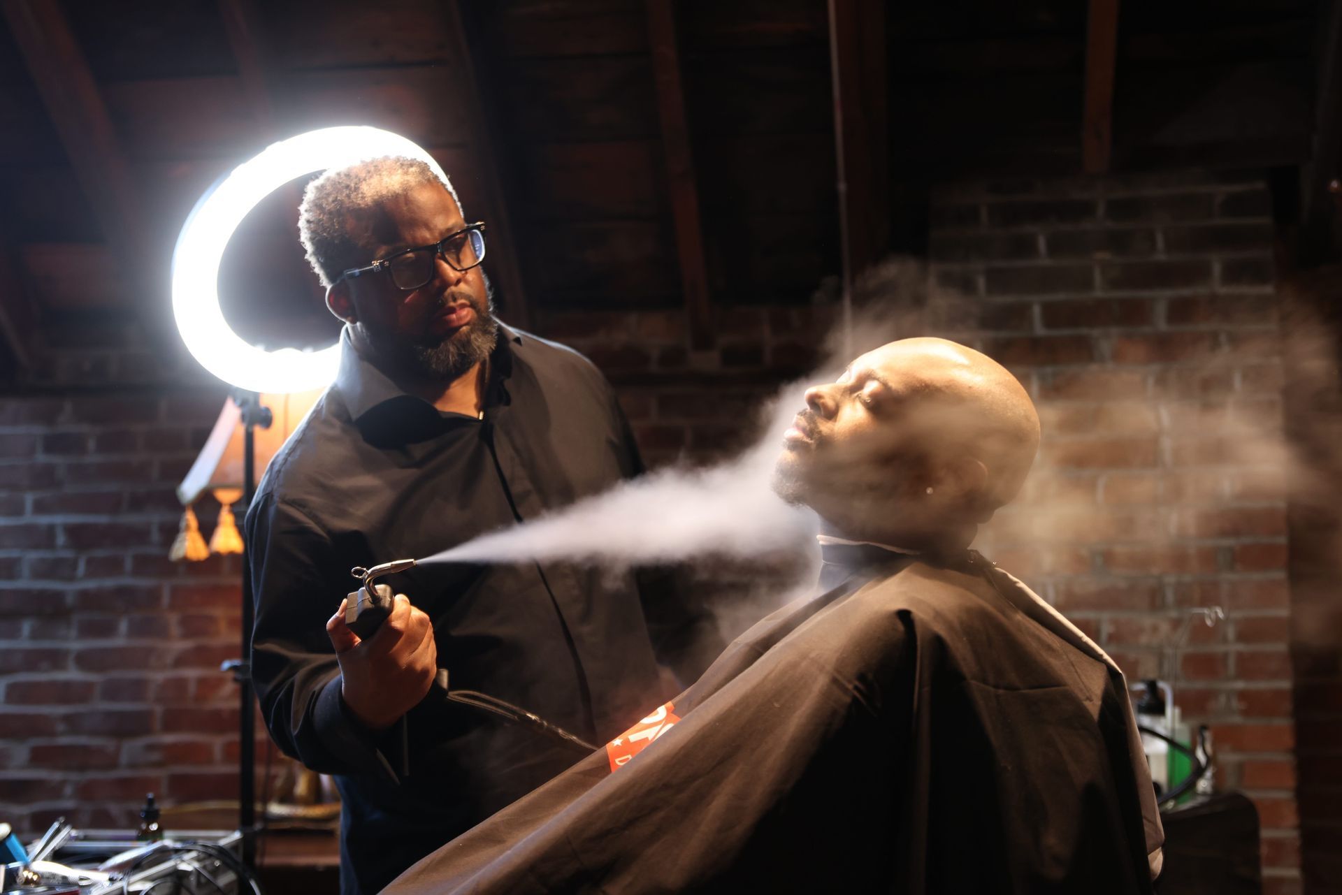 Barber cutting a client's hair with mist spraying in a dim barbershop