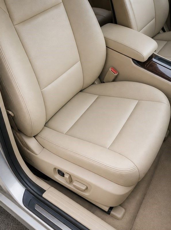 Beige leather car front seat with power controls and red seatbelt buckle, viewed from the side