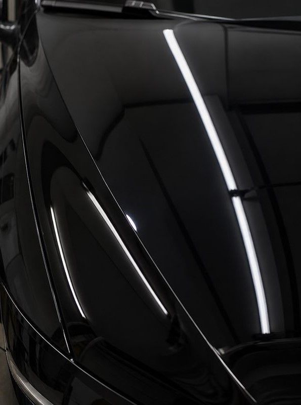 Close-up of a glossy black car hood with bright white reflections from overhead lights