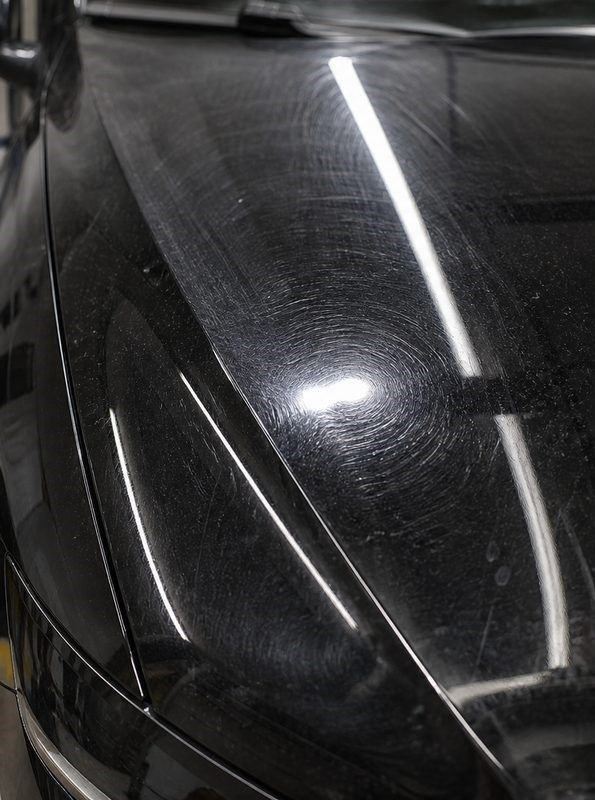 Close-up of a black car hood with glossy reflections and visible swirl marks