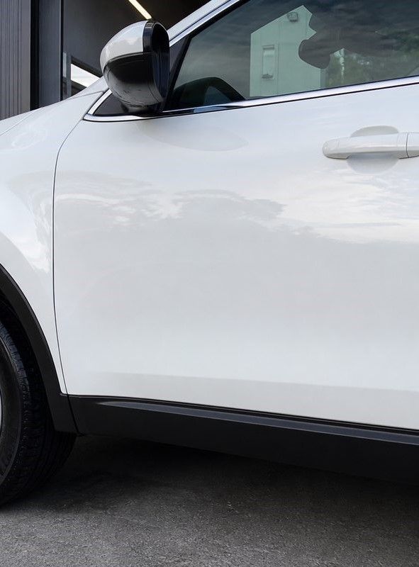 Close-up of a white car’s side door and mirror parked on pavement.