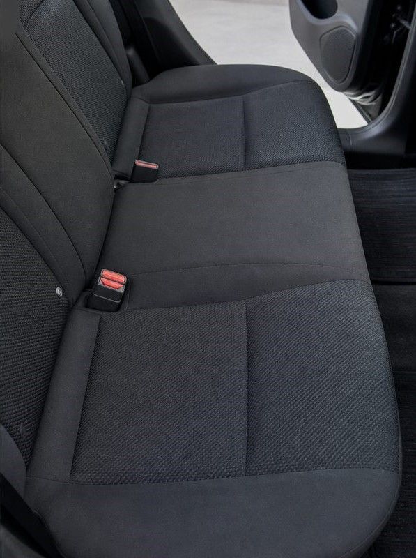 Black cloth back seat of a car with seat belts visible and a door open on the right.