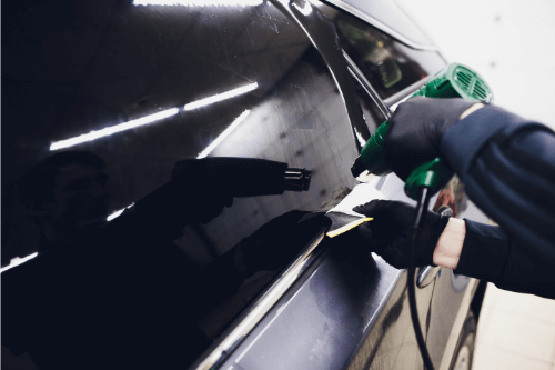 Person polishing a black car door with a green cloth and tool in a garage