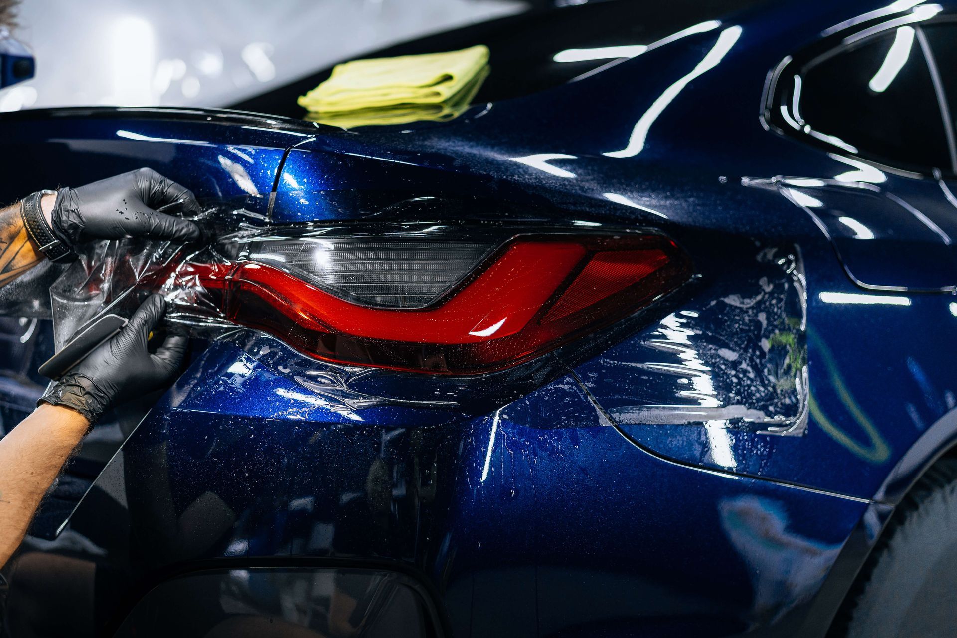 Person polishing a blue sports car’s rear taillight with a cloth