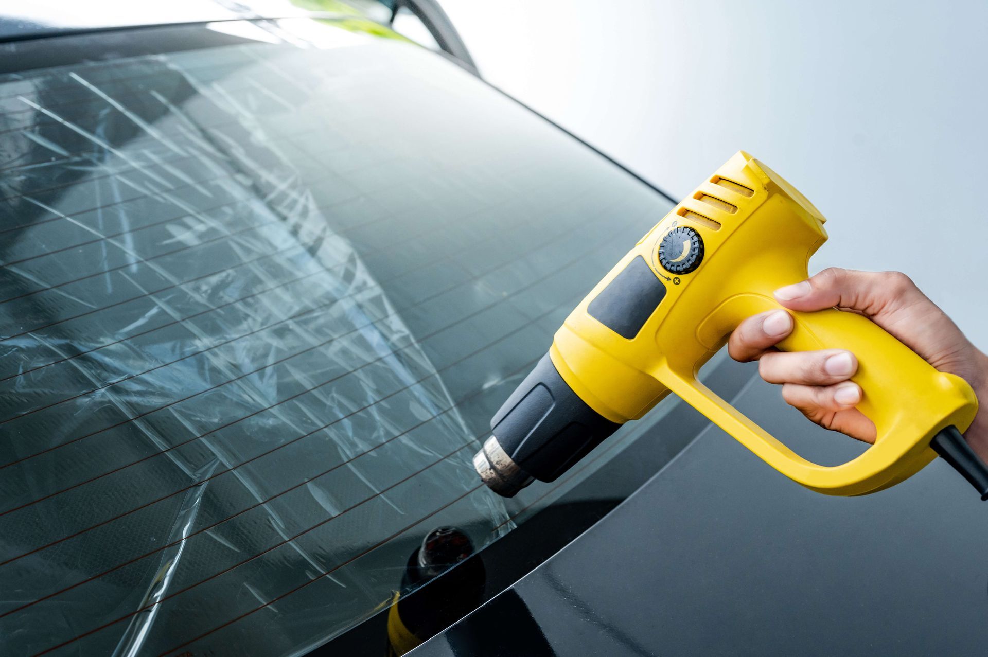 Yellow heat gun removing cracked windshield glass on a car