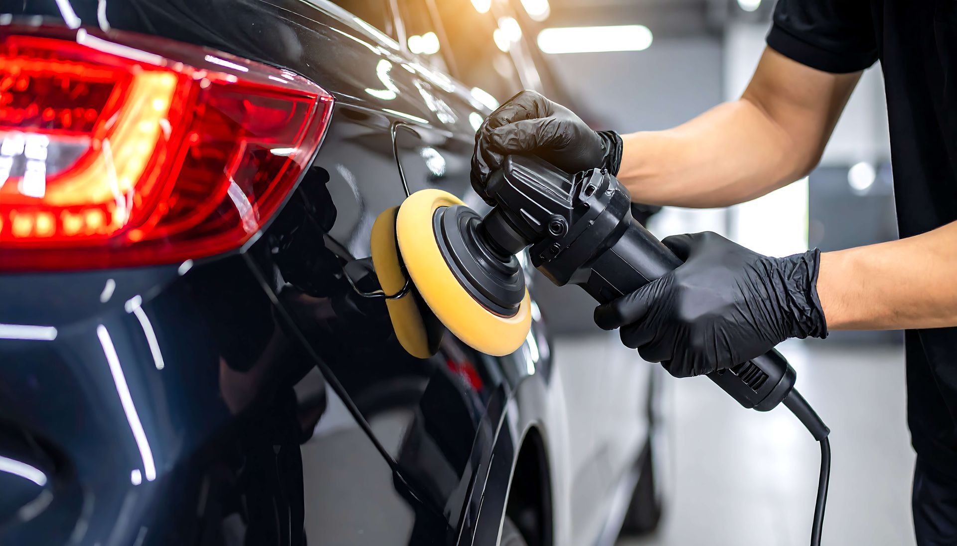 Gloved person polishing a black car with a buffer in a garage