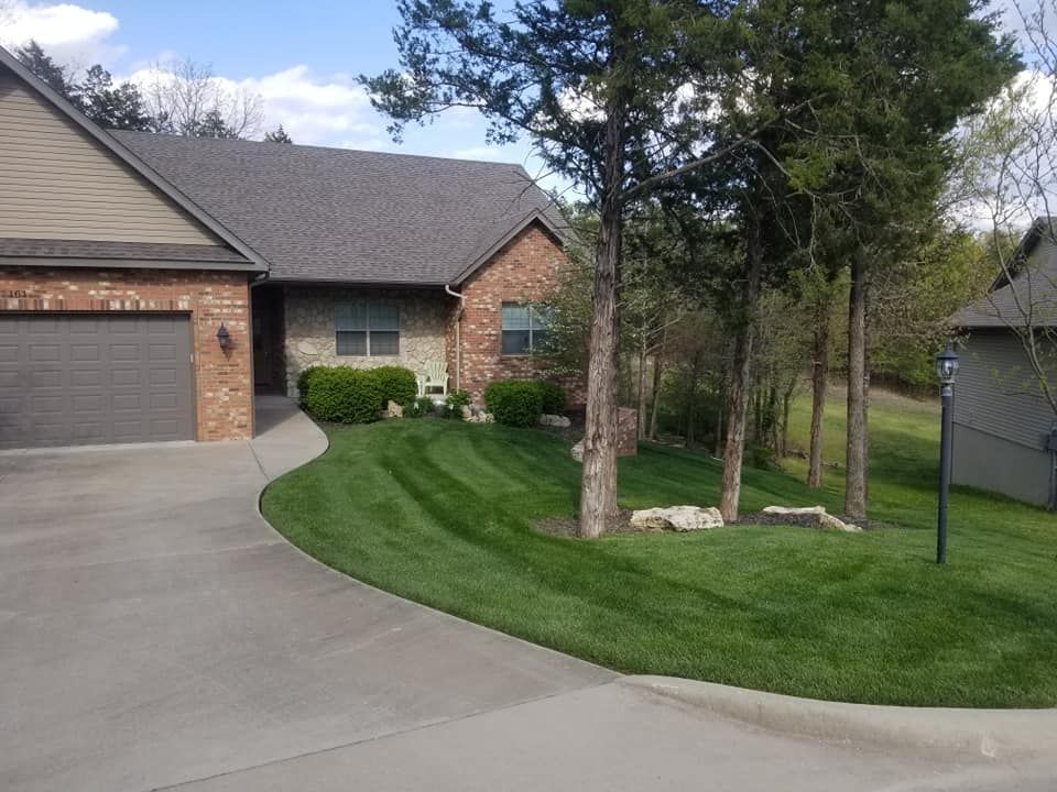 House with brick facade, attached garage, and lush green lawn with freshly cut stripes.
