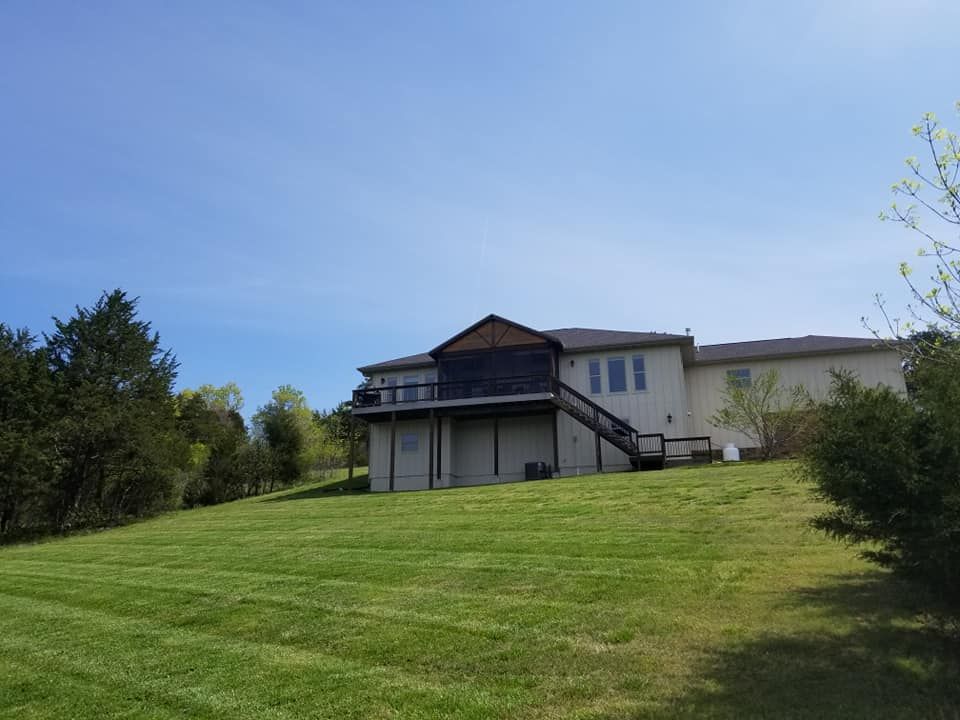 Beige house with a deck on a grassy hill under a blue sky.