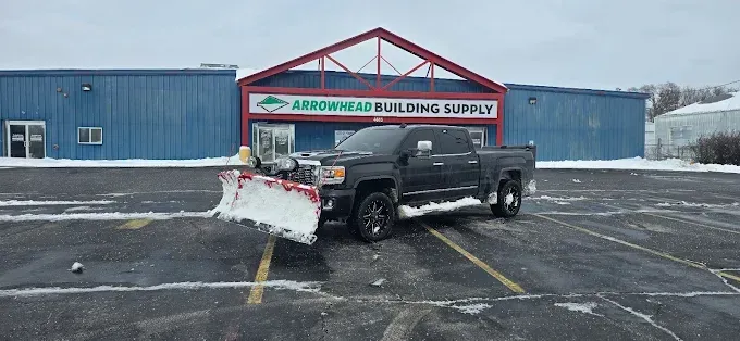 A snowplow truck clearing the parking lot in front of a building supply store on a snowy day.
