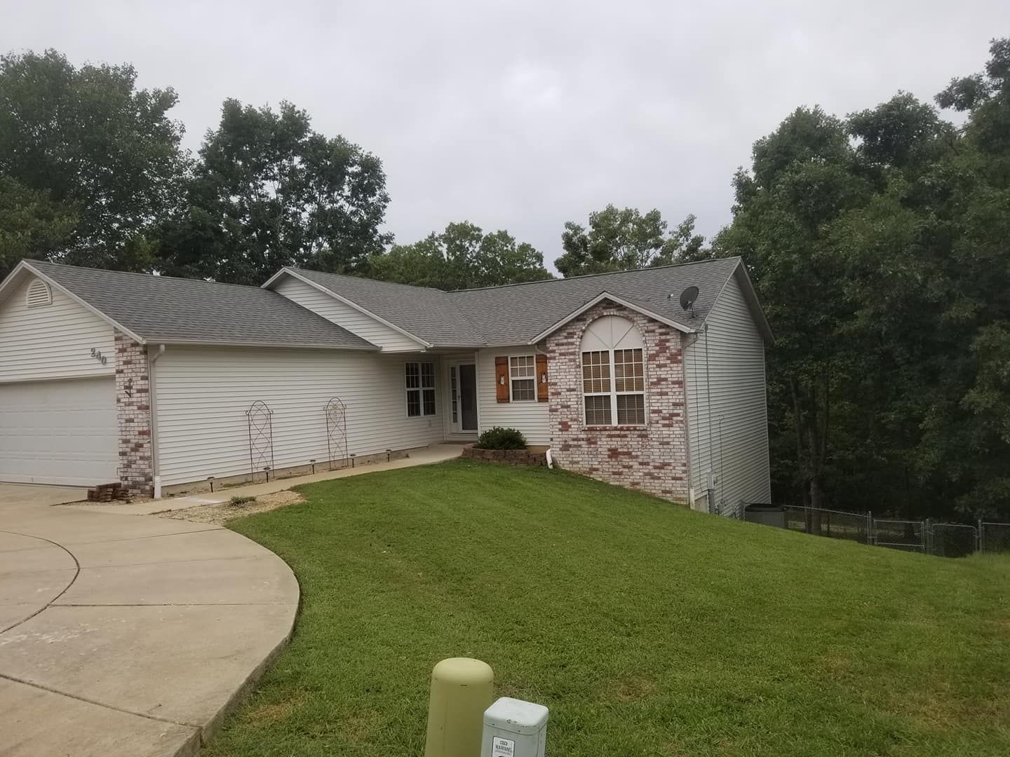 A one-story house with a brick facade, gray roof, and green lawn on a cloudy day.