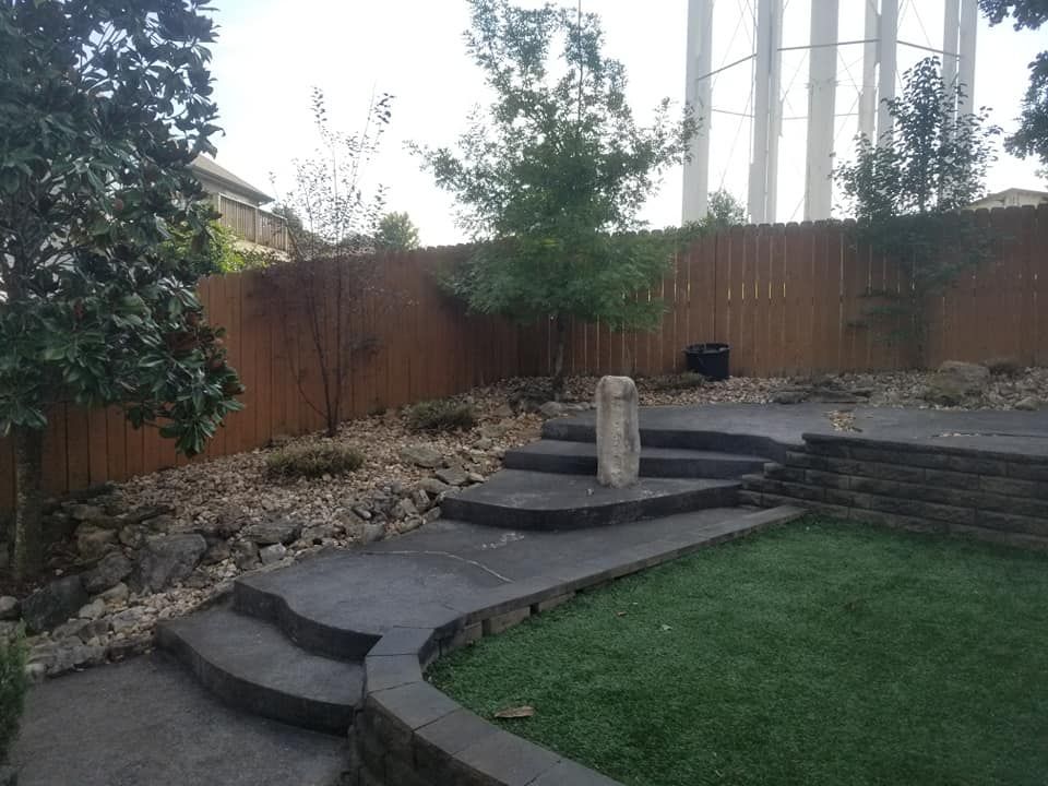 Concrete steps and pathway lead up a sloped yard with a rock garden and brown wooden fence.