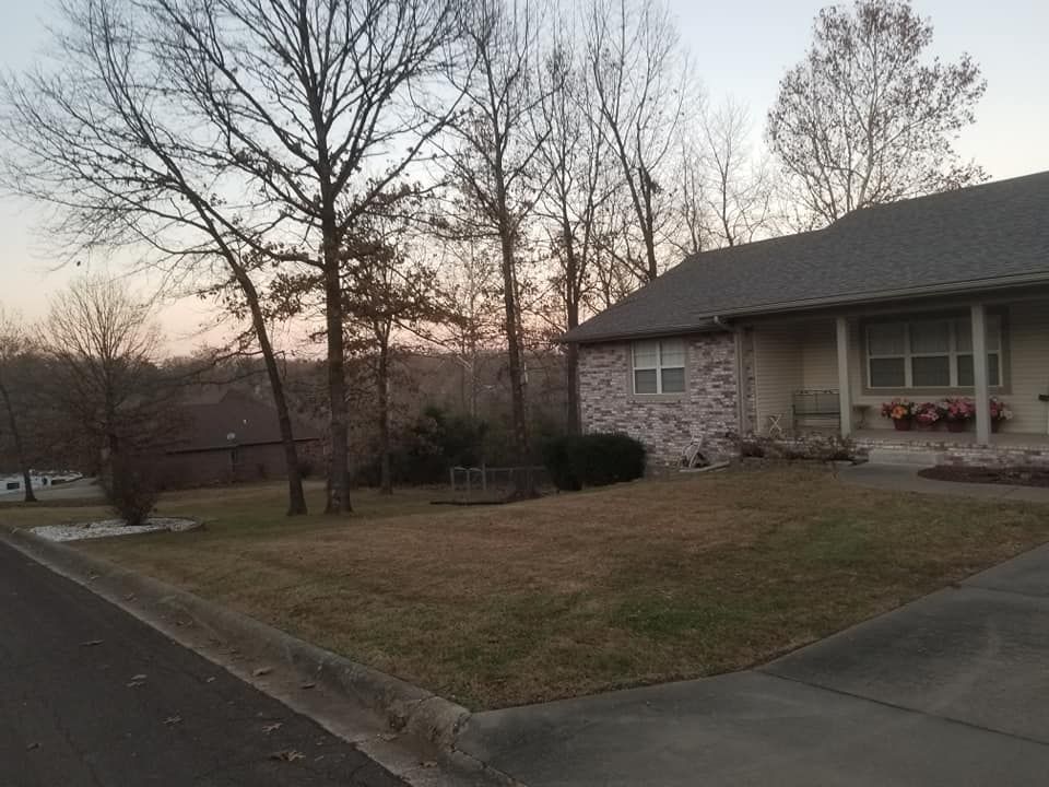 House with brick siding and a yard, trees and sunset in background.