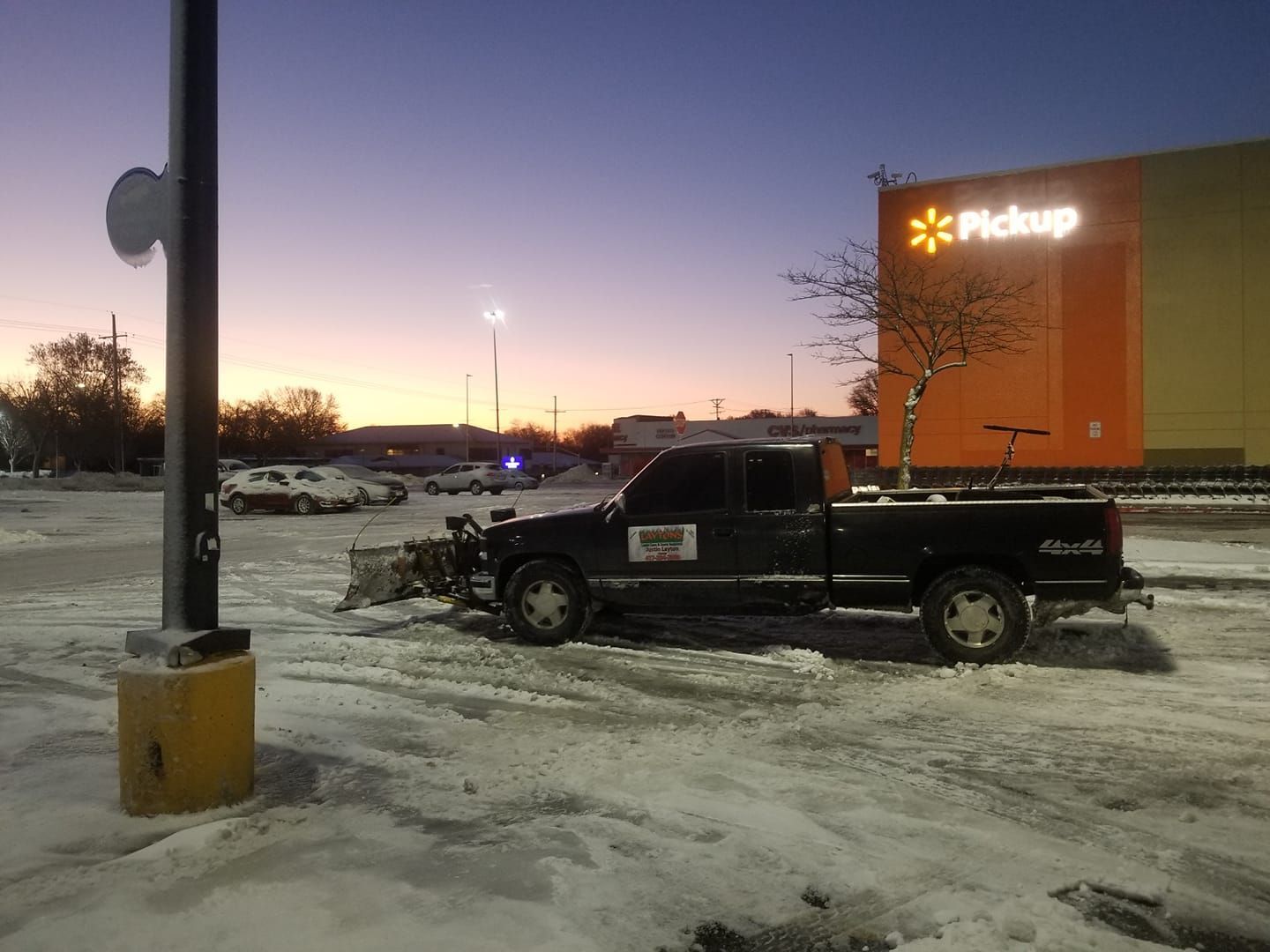 Snow-covered Walmart parking lot with a plow truck at dawn. 