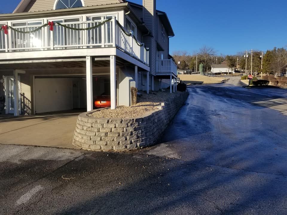 Gray house with a garage and a brick retaining wall next to a paved driveway.