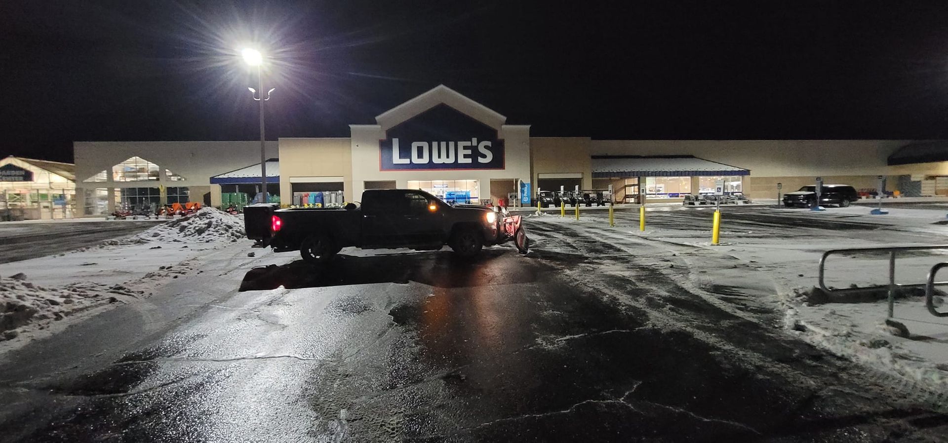 A truck parked in front of a Lowe's store at night, with snow on the ground and lights overhead.
