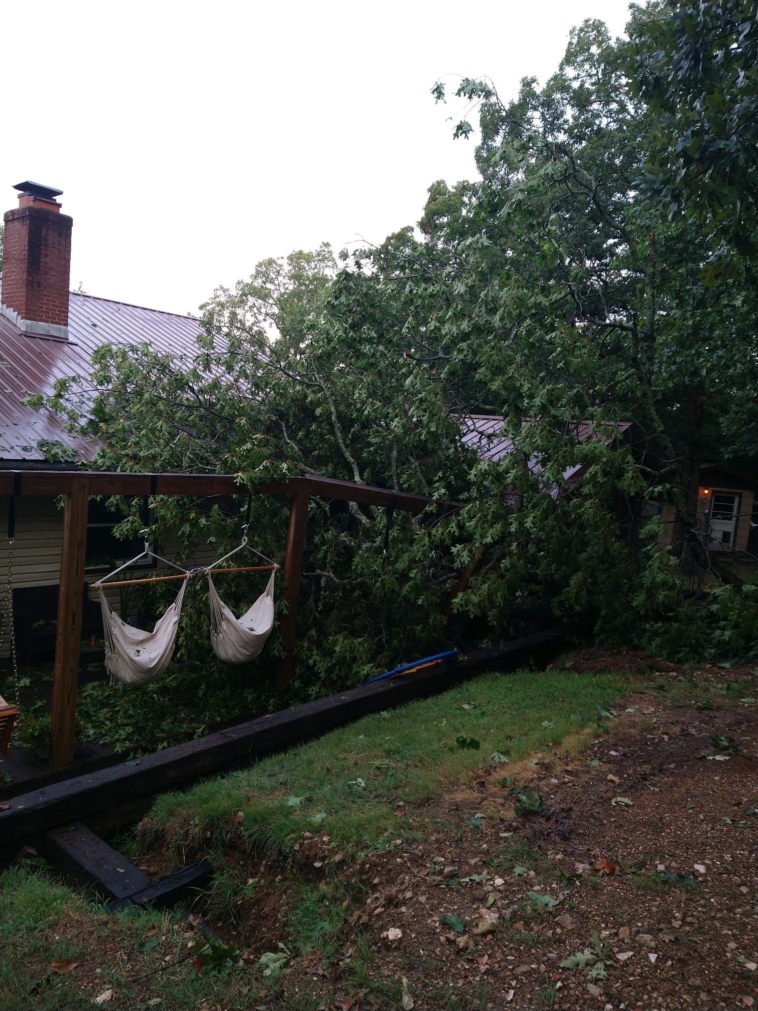Tree branches fallen on a swing set and building, in a yard.