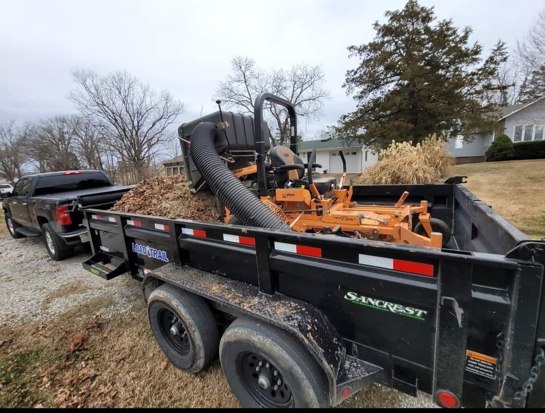 Black truck towing a trailer loaded with leaves and lawn equipment, parked next to a curb.