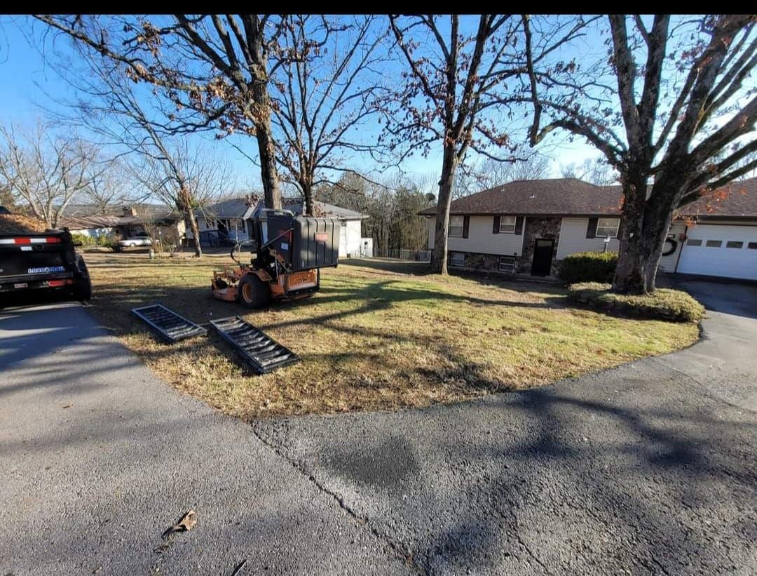 A skid steer and ramp on a lawn in front of a house on a sunny day.