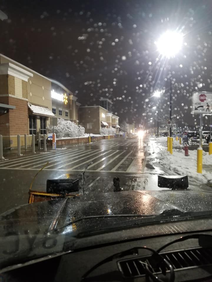 Snow-covered Walmart parking lot at night; a snowplow clearing the road.