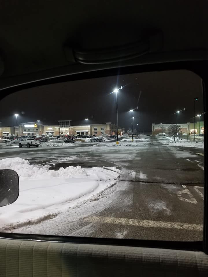 Snowy parking lot at night, lined with shops under streetlights.